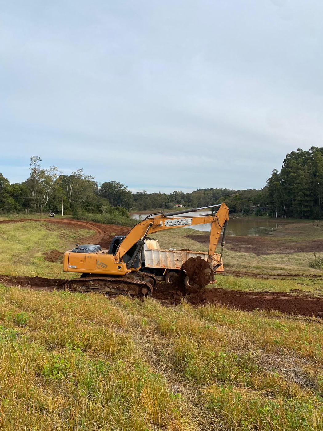 Escavadeira removendo a camada de vegetação em limpeza de terreno rural em Passo Fundo, com caminhão caçamba recebendo o material
