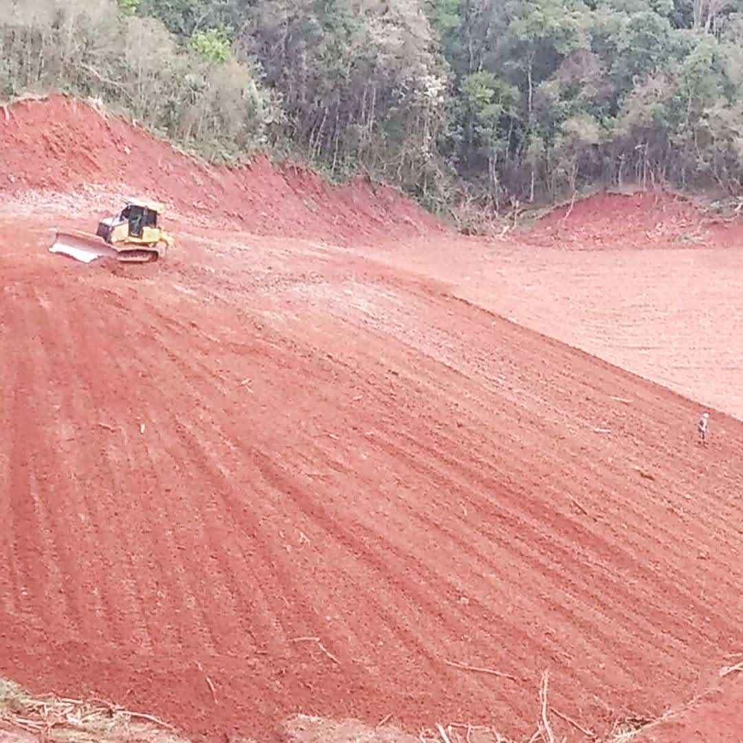 Trator esteira nivelando grande área em terreno de declive, com talude conformado ao fundo